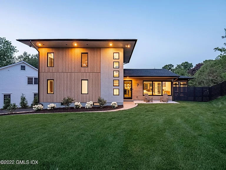 Exterior of modern with a large two-story section and a smaller one-story section. Both sections have a lot of windows. There's a paved path curving to the front door and a sloping green lawn in front.